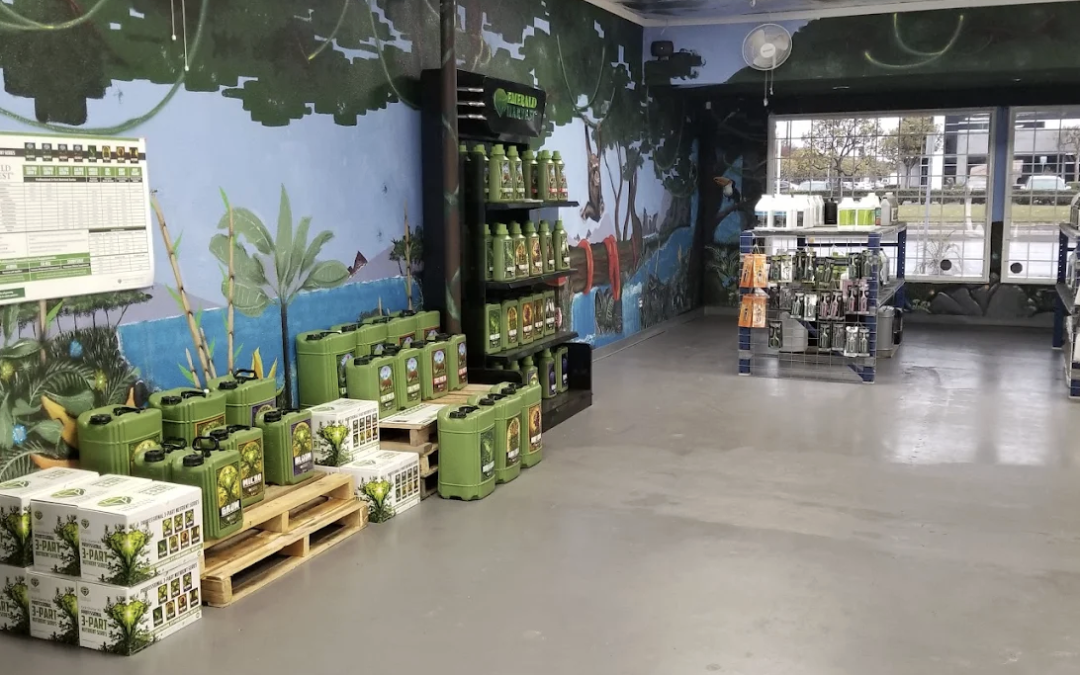 A store with green gardening products on pallets, shelves, and racks, beside a wall with a nature mural.